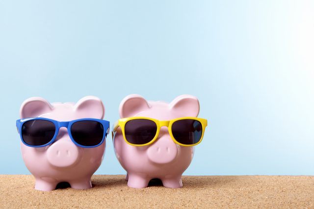 Two pink piggy banks on a beach with sunglasses. Space for copy.